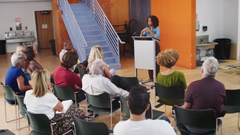 woman at podium chairing neighborhood meeting in community centre