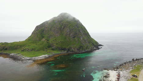 aerial footage of vik beach and hauklandstranda norway, large mountain in the ocean with a small boat in the water