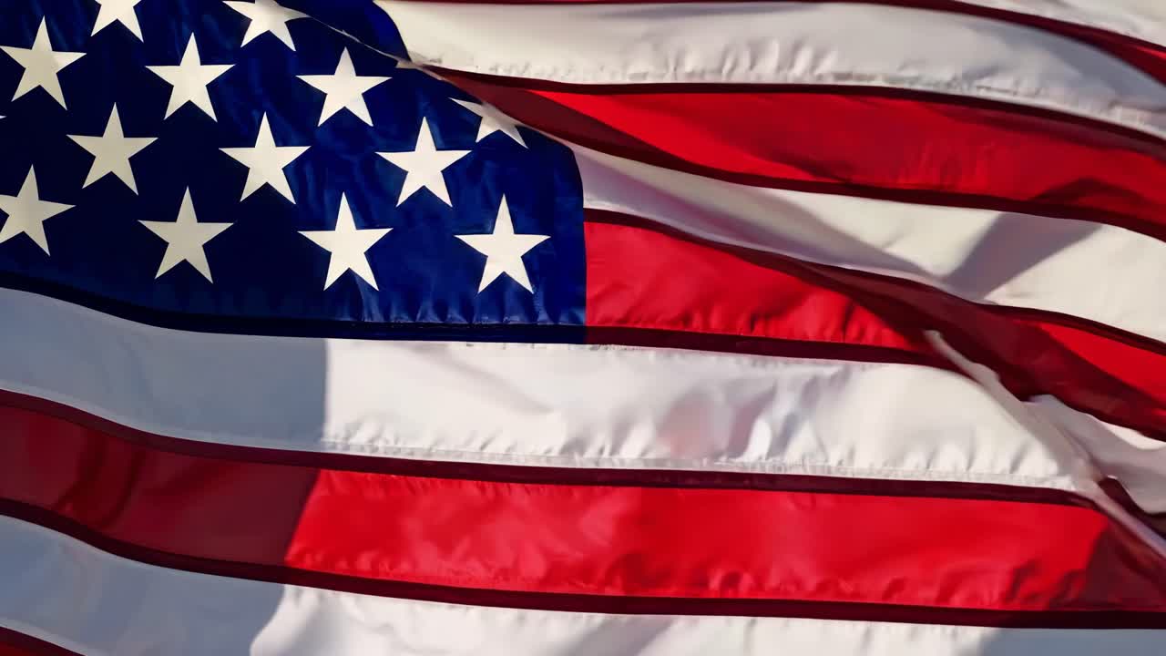 A low-angle video shot of the American flag waving against a clear blue sky, emphasizing patriotism
