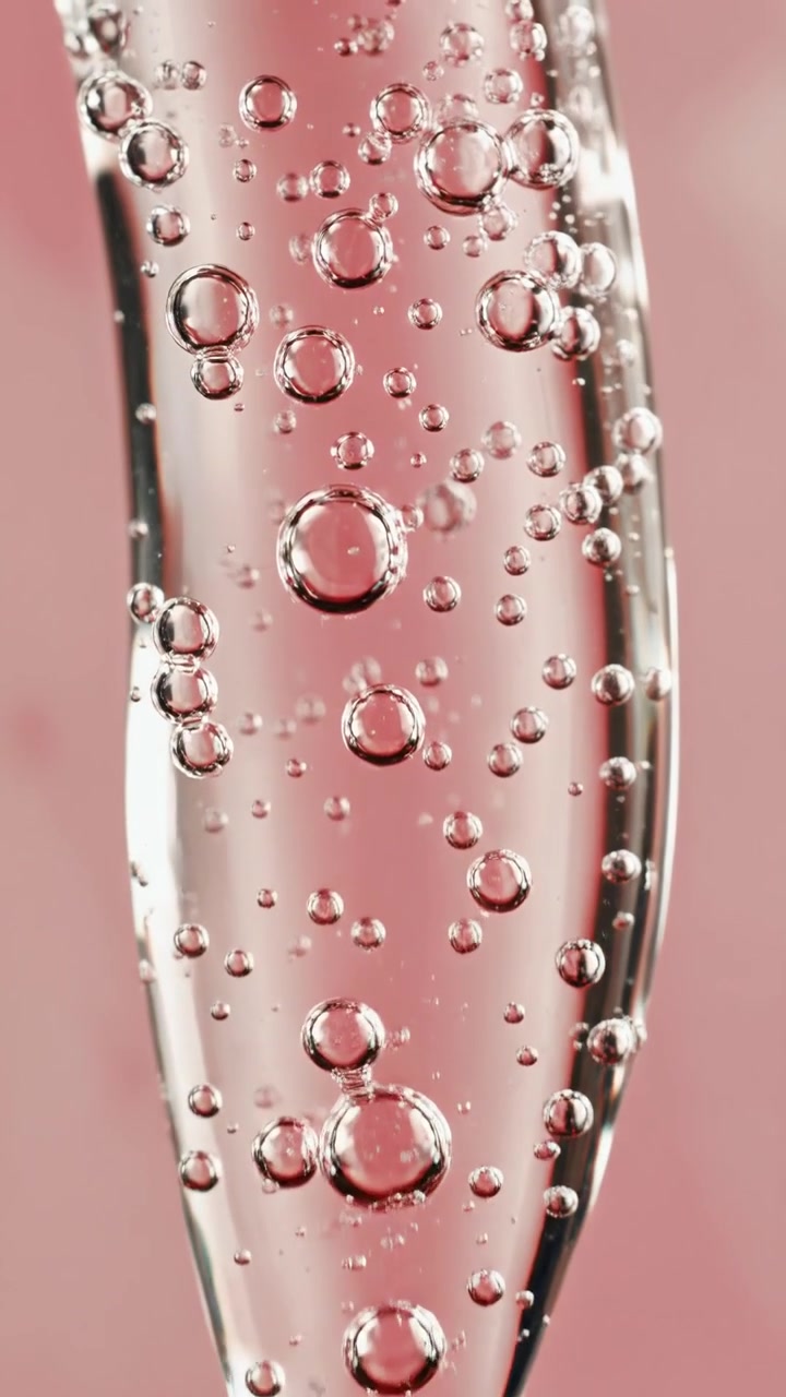 Primer plano de gel cosmético transparente con microburbujas de aire sobre un tubo aplicador de vidrio contra un fondo rosa