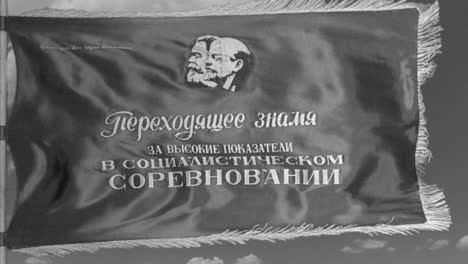 in the style of a black and white newsreel, a soviet flag depicting marx and lenin flies in slow motion