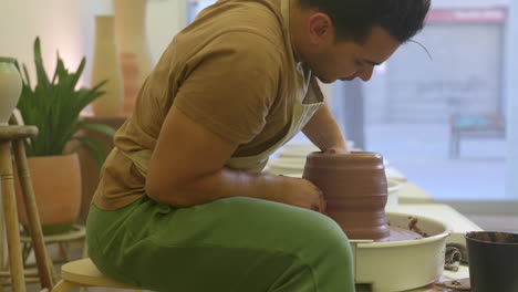 potter sitting working clay and moulding pottery on turntable in studio workshop