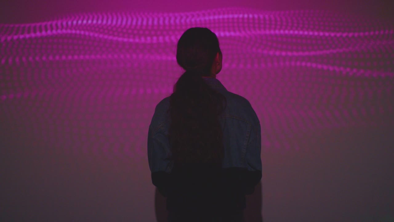 mujer visitando una exposición de arte inmersiva con proyección de formas y patrones en la pared 7