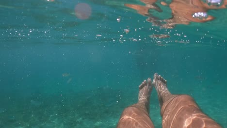 under water personal perspective view of man legs floating in clear transparent sea water beneath surface, slow motion