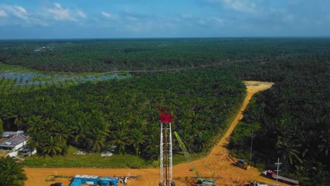 cinematic onshore drilling and workover rig structure and rig equipment for oil exploration and exploitation in the middle of jungle surrounded by palm oil trees during sunset time