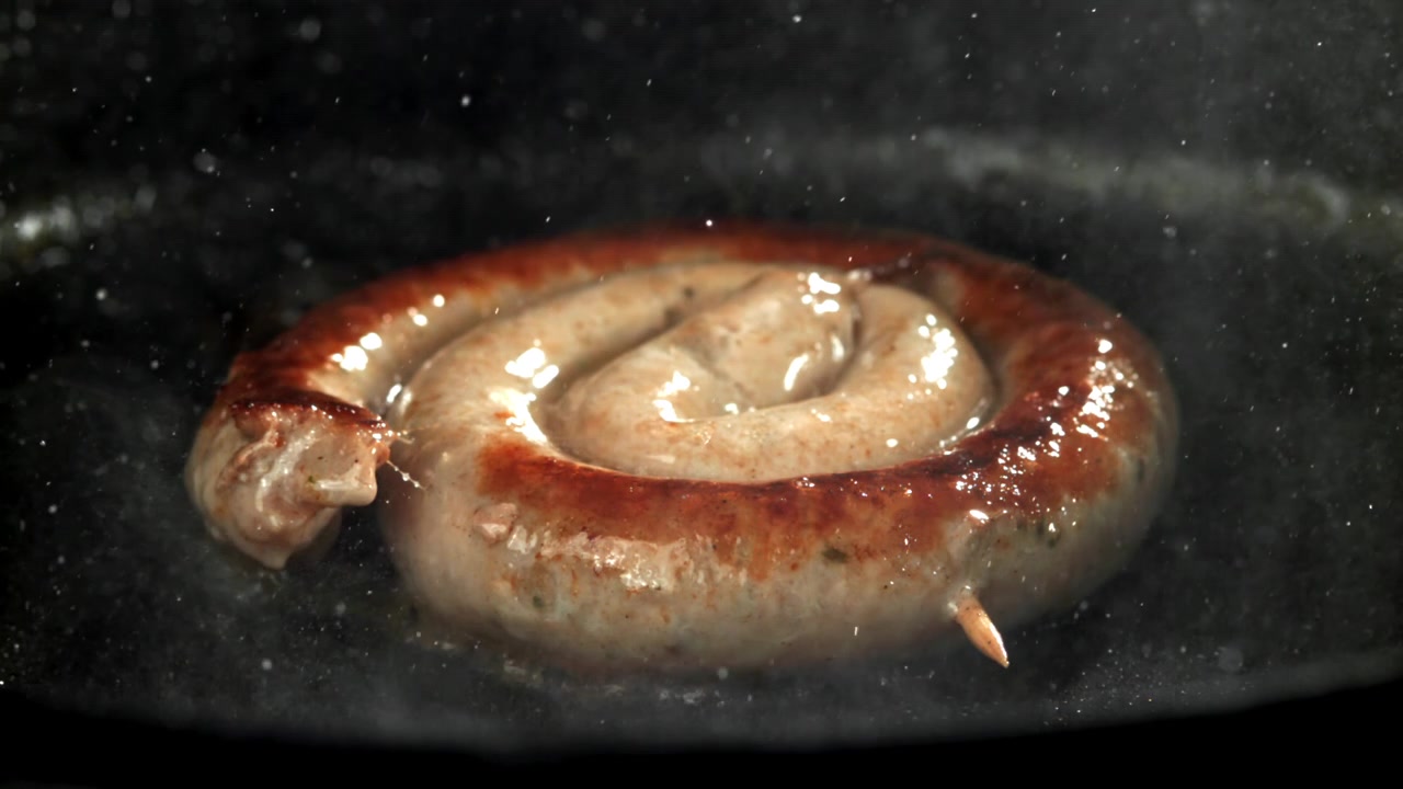 Närbild på en spiralformad korv som steker i en het panna