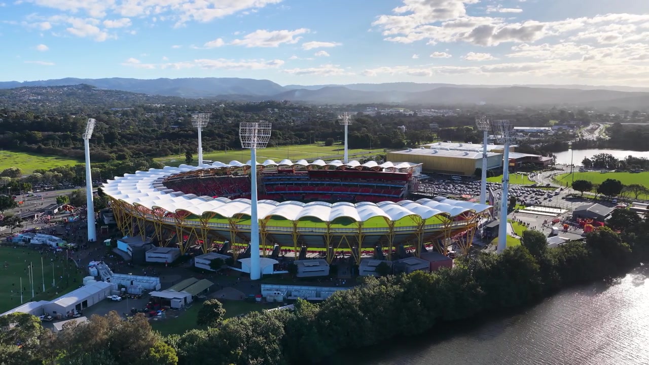 Wide aerial shot of a circular sports arena under bright daylight with surrounding green landscape.