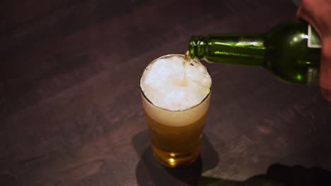 man's hand pours a beer from the green bottle into a glass, close-up shot from the top