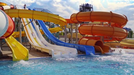 People ride down from colorful water slides. Beautiful water splash in the outdoor pool. Family entertainment in summer. Slow motion.
