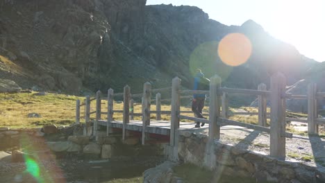 un excursionista en solitario caminando a través del puente de madera en cima fontana en valmalenco con brillantes llamaradas solares en la lente