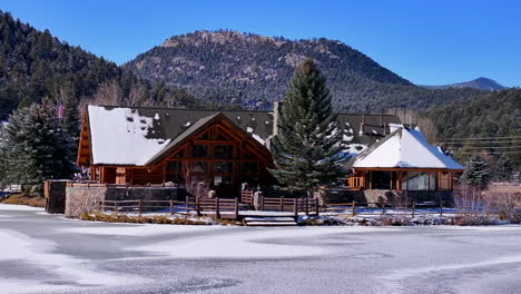 First-snow-ice-frozen-covered-white-Evergreen-Lake-House-Rocky-Mountain-landscape-scene-morning-front-range-Denver-aerial-cinematic-drone-Christmas-ice-skating-hockey-blue-sky-slow-backward-motion