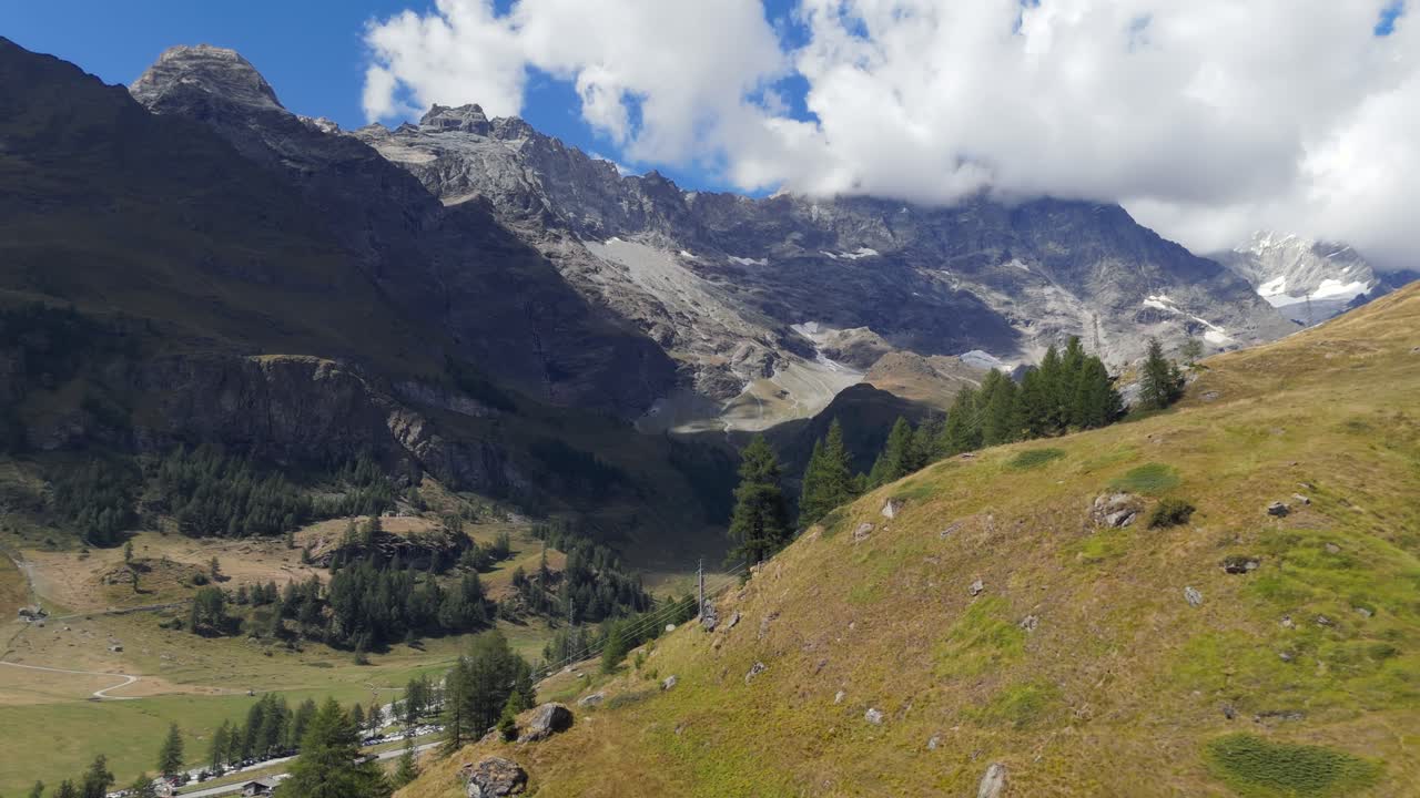 Ripresa aerea con drone che avanza verso le montagne di Valtournenche, Italia, con alberi di pino durante una giornata di sole e atmosfera limpida