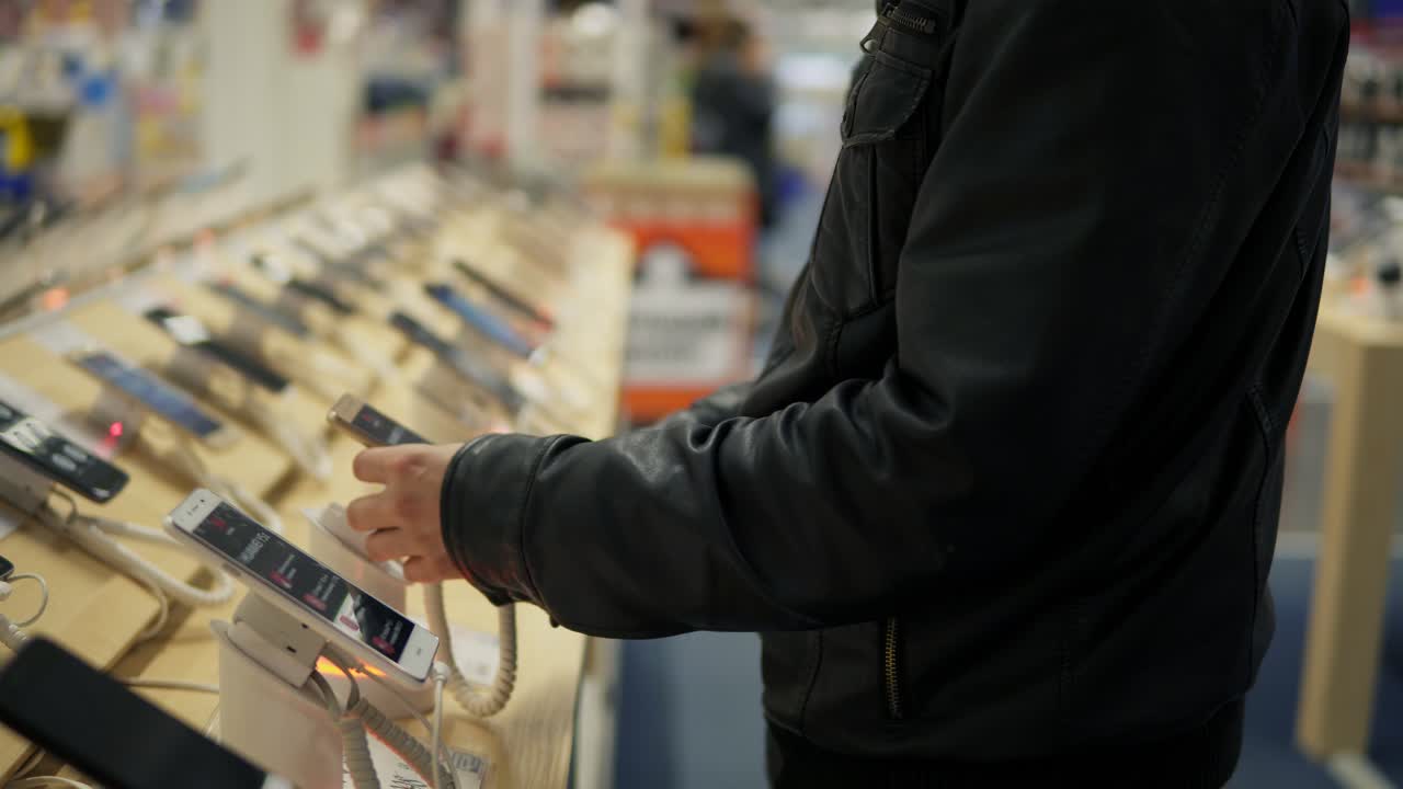 Closeup view of a young man's hands choosing a new mobile phone in a shop. He is trying how it works