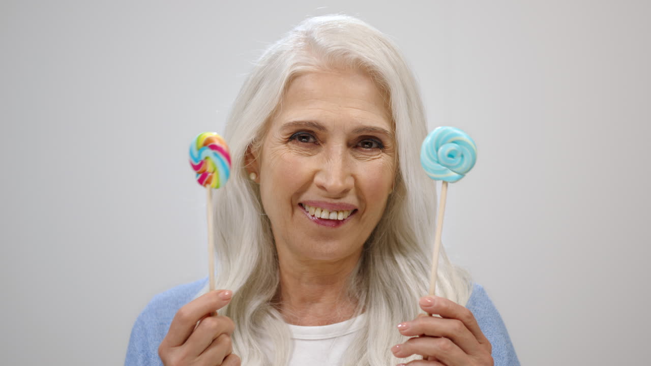 Anziana allegra che tiene una caramella in studio. Signora anziana felice che si diverte al chiuso.