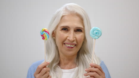 Cheerful-old-woman-holding-candy-in-studio.-Happy-aged-lady-having-fun-indoors.