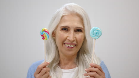 cheerful old woman holding candy in studio. happy aged lady having fun indoors.