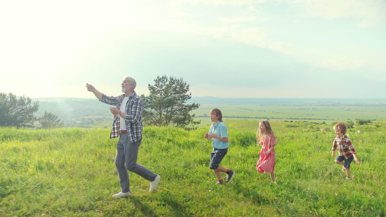화창한 날에 연을 날리는 동안 공원에서 손자들과 함께 달리는 백인 노인의 측면
