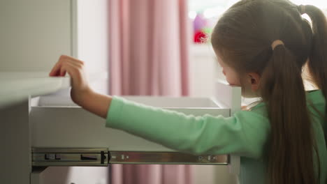 curious little girl opens desk drawer in children room