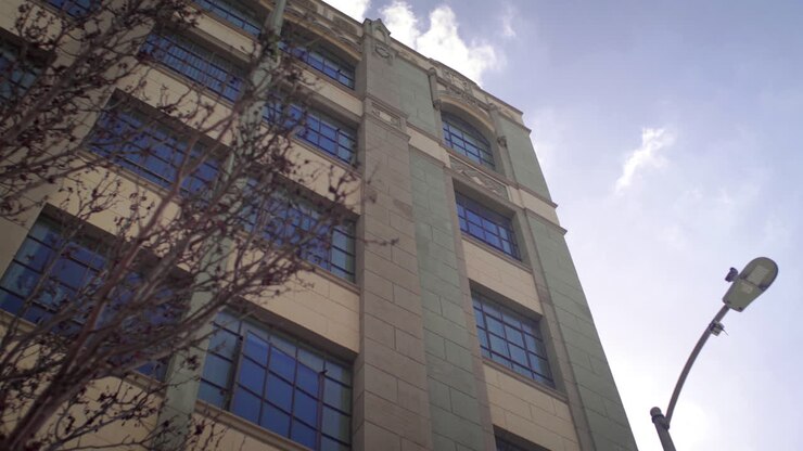 Vista em ângulo baixo de um edifício moderno com poste de luz contra um céu nublado com reflexo solar.