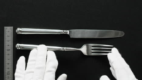 minimalist table setting with white plate, fork, and knife arranged neatly, and a gloved hand adjusting cutlery.