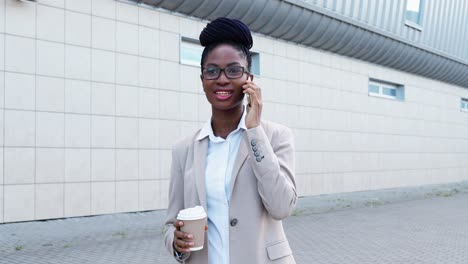 african american businesswoman in stylish clothes and glasses talking on the smartphone in the street