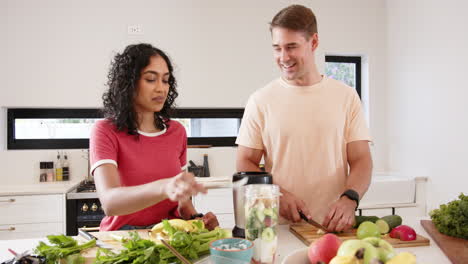 preparing healthy smoothie, young multiracial couple chopping fruits and vegetables, at home