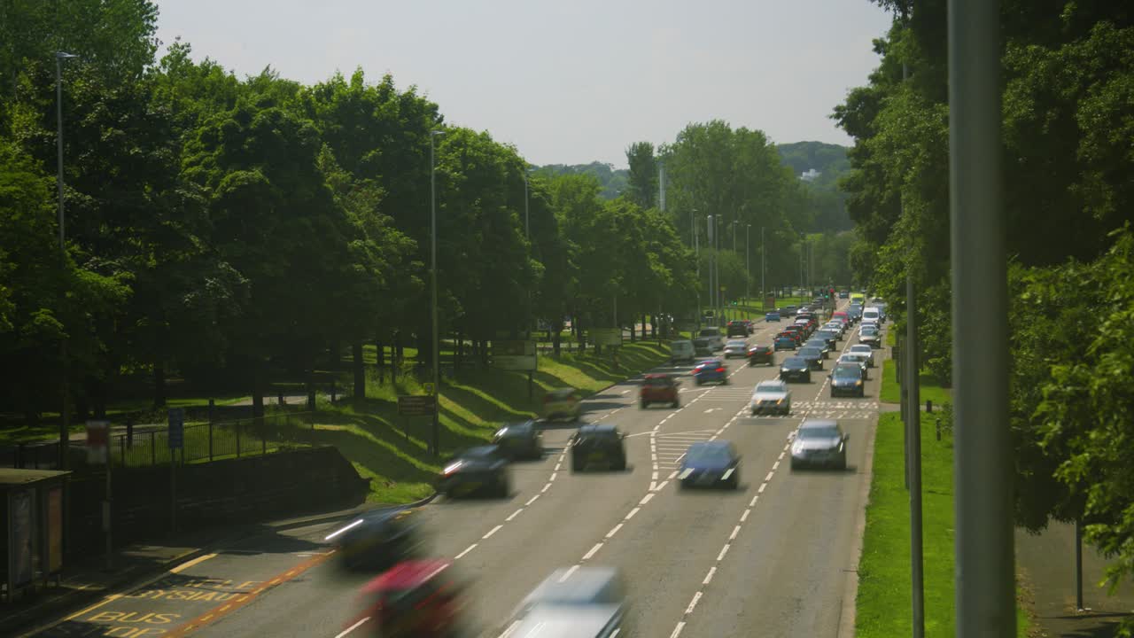 Timelapse of Busy Traffic Queues Stopping and Starting at Lights Along Busy City Road in Swansea with Trees Lining Roadside