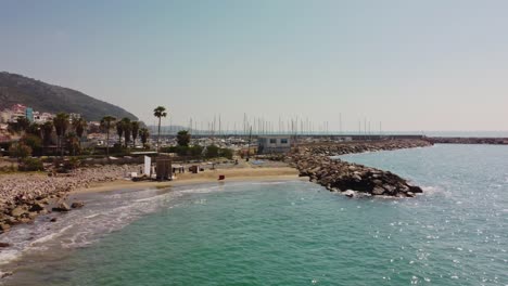 Garraf-coast-in-barcelona,-sunny-day-with-clear-blue-waters-and-boats-docked-at-marina,-aerial-view