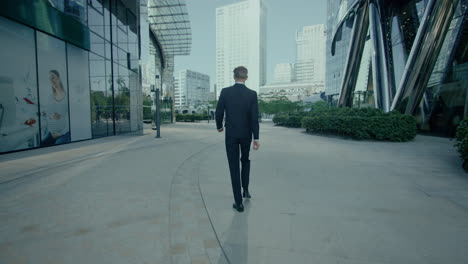 view from behind of man in black suit walking outside then happy jumping, cinematic tracking shot