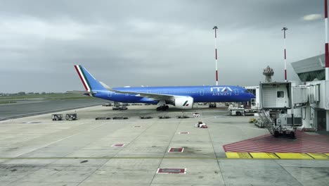 italian airways jet parked at boarding gate under an overcast sky, surrounded by ground service vehicles and baggage carts, showcasing air travel logistics and airport operations efficiency