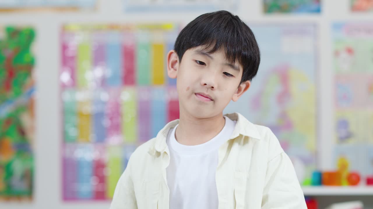 Young boy smiles and holds blue foam number four in brightly lit classroom, front view