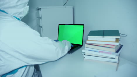 Hospital-Worker-In-Full-PPE-Suit-Working-On-A-Laptop-With-Green-Screen---medium-shot