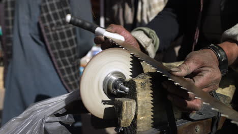 pedal knife sharpener with person sharpening hacksaw on sidewalks of bamyan, afghanistan