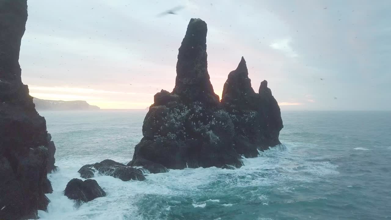 reynisdrangar скалы на пляже reynisfjara рядом с vik i myrdal в южном исландии. воздушный дрон выстрел летит над скалой во время восхода солнца. большие штормовые волны разбиваются с скалой. кадры высокого разрешения. 4k