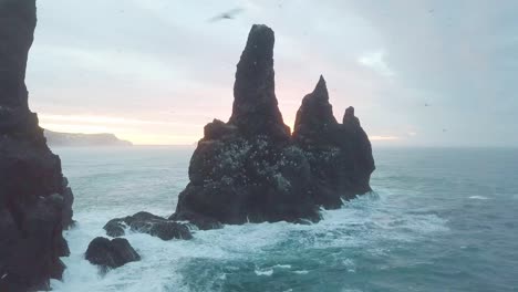 reynisdrangar rocks at reynisfjara beach next to vik i myrdal at south iceland. aerial drone shot flying over a cliff during sunrise. large storm waves crash rock. high resolution footage. 4k