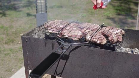 Meat-grilled-on-the-grid.-Food-for-barbecue-party.-Male-hand-is-splashing-water-to-eliminate-fire.-Meat-on-a-grill.-shot-in-4k