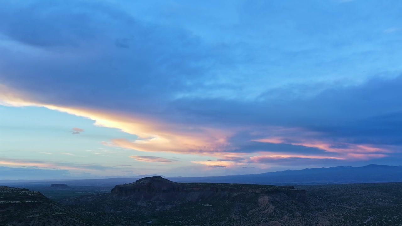 4K UHD drone timelapse from a vast canyon overlook. Heavy twilight clouds shift to display glowing sunset colors, casting dynamic shadows over the deep gorge and distant mountain horizon.