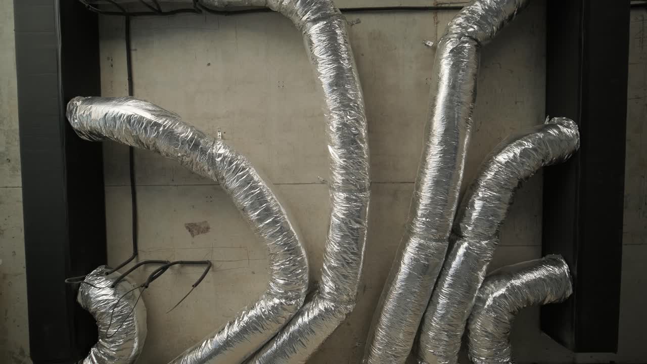 Multiple insulated flexible air ducts installed inside a modern building, with a focus on the metallic surface and bends against a concrete wall
