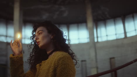 woman holding a lit match in a dim, industrial setting
