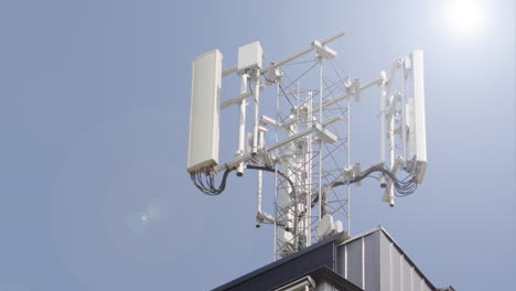 tele shot of 5g mobile phone mast atop building against bright blue sky