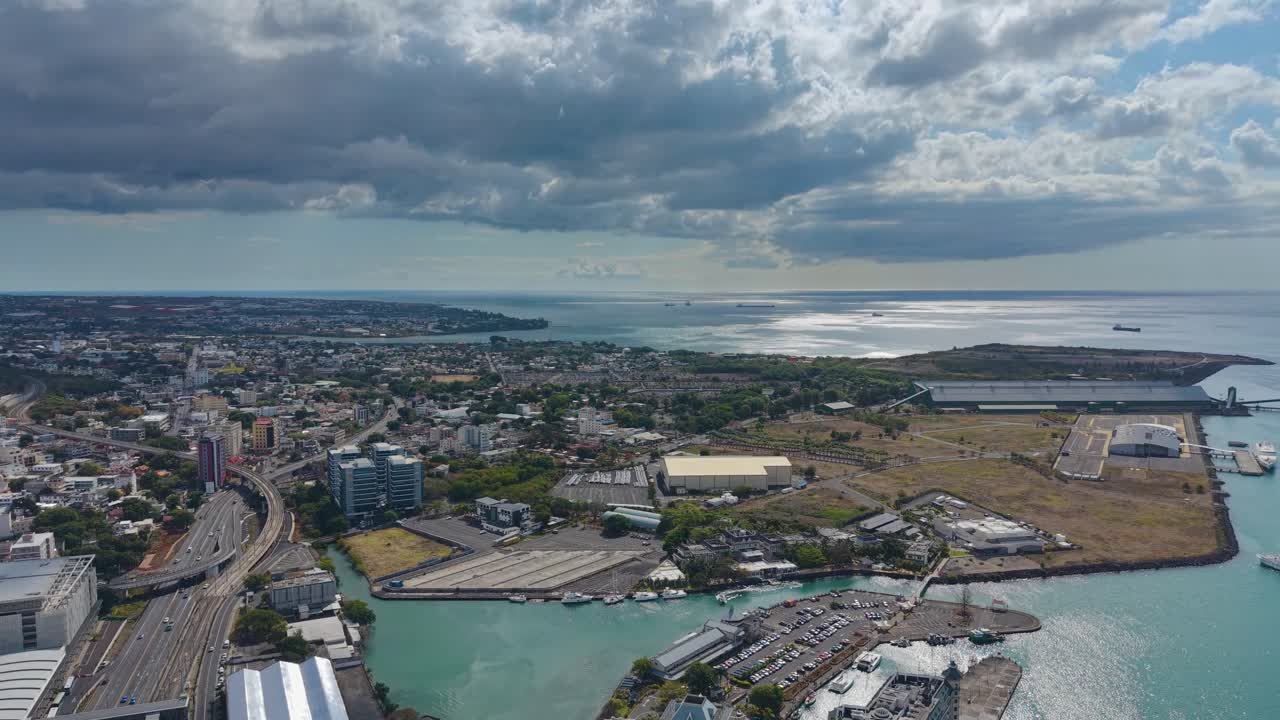 Rotating aerial view of Port Louis, Mauritius, showing the city skyline, harbor, and surrounding hills under dramatic clouds, blending coastal charm with urban life