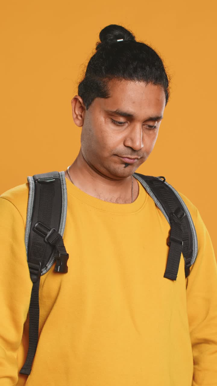 Young Man with Backpack Looking Thoughtfully on Yellow Background