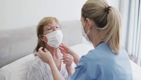 Female-health-worker-putting-face-mask-on-senior-woman-at-home