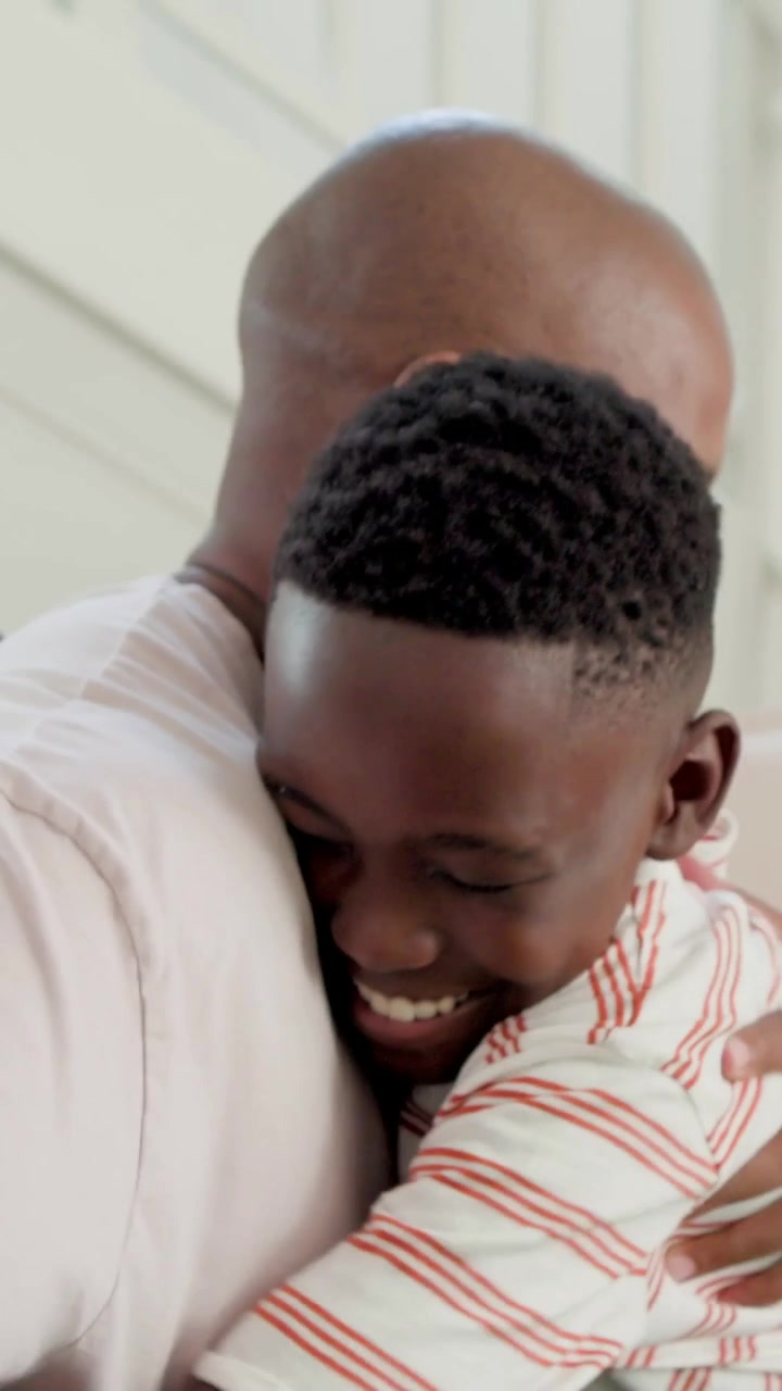 Vertical video: Hugging son starting hug, dad hugging back on sofa at home, pillows, showing love