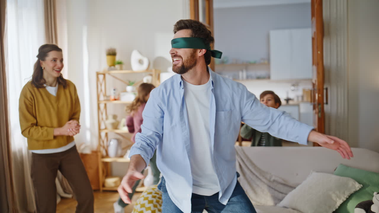 Playful father catching mother wearing blindfold hugging living room closeup