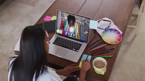 mujer afroamericana escribiendo notas de memoria mientras tiene una videollamada en una computadora portátil en casa