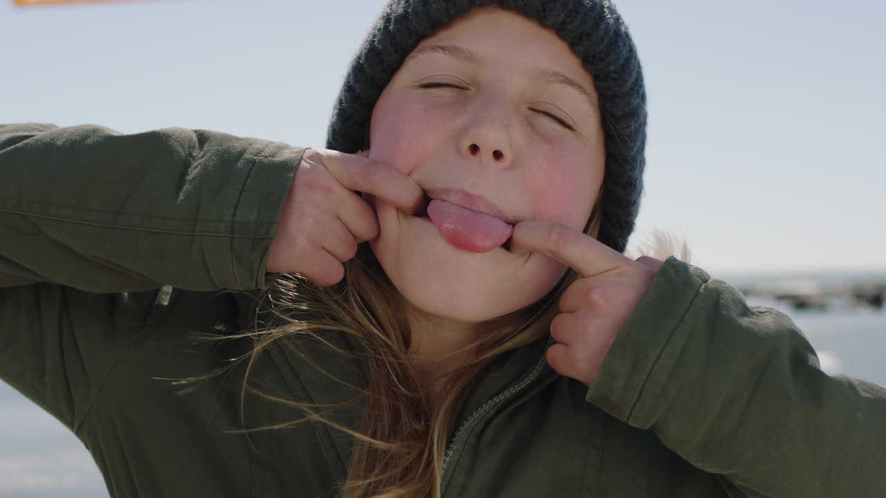 retrato de una chica feliz en la playa posando haciendo caras riendo con abrigo y gorra