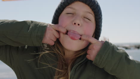 Retrato-De-Niña-Feliz-En-La-Playa-Posando-Haciendo-Muecas-Riendo-Vistiendo-Abrigo-Y-Gorro