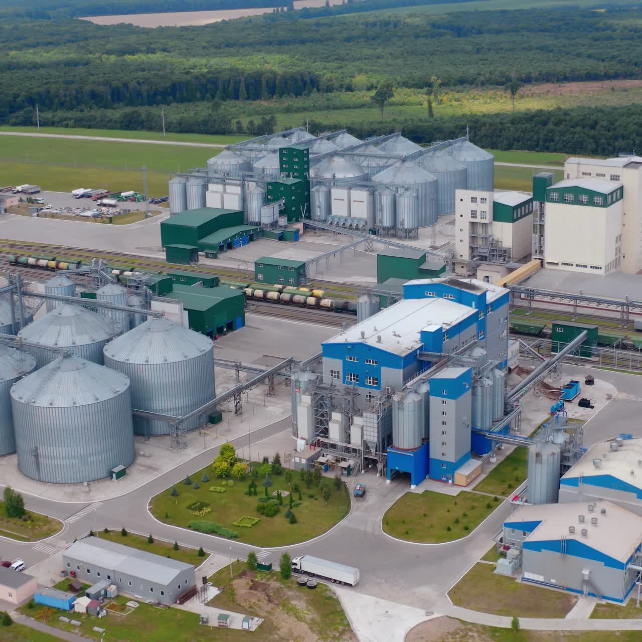 Beautiful agriculture complex among green landscape. Grain elevators and modern buildings of a grain drying factory. Aerial view