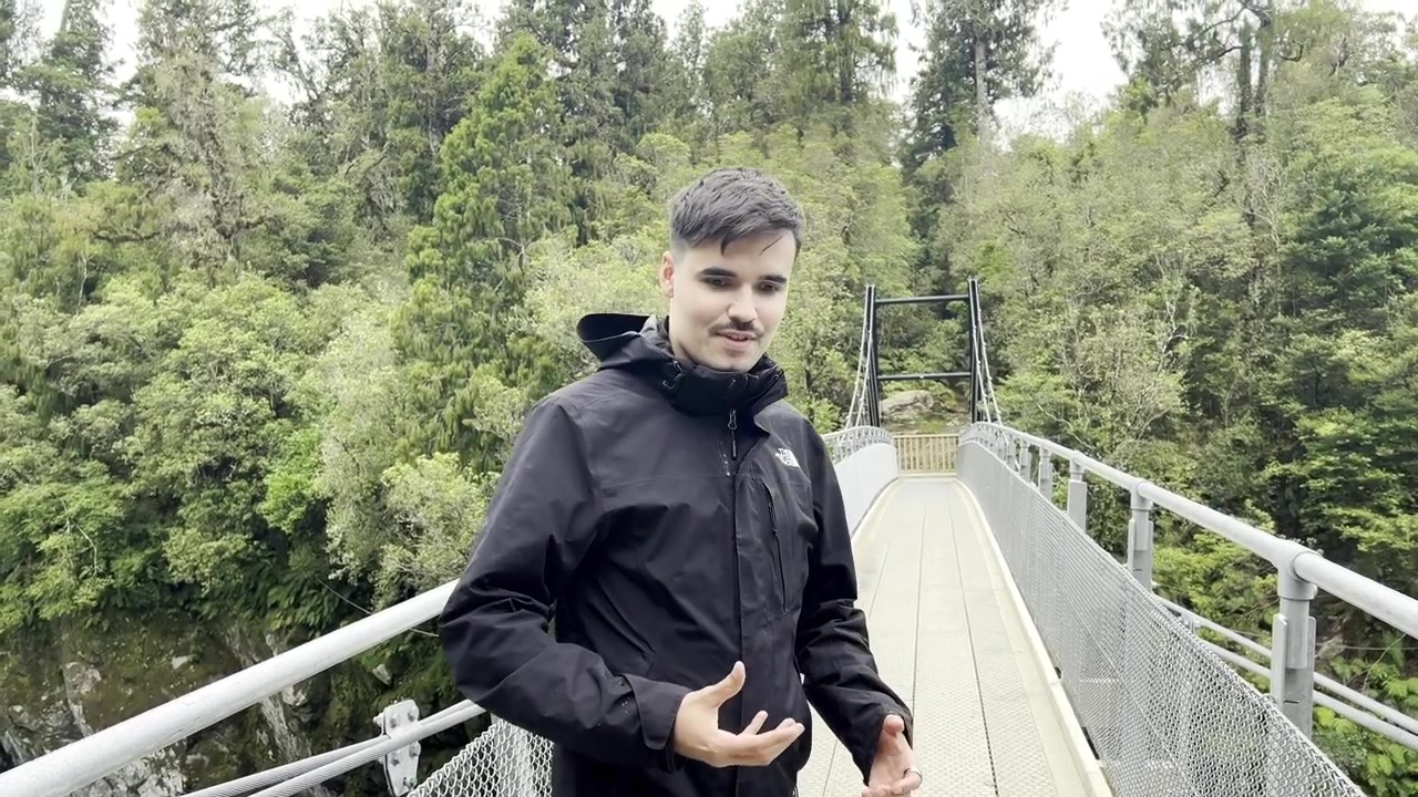 A man gestures while standing on a suspension bridge over a river